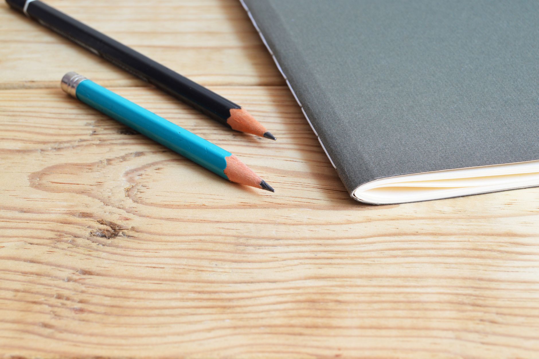 Composición minimalista de un cuaderno y lápices sobre un escritorio de madera.